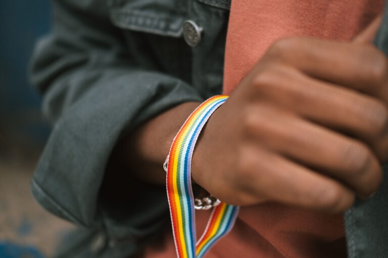 Crop anonymous African American male in casual clothes wearing gay pride bracelet and touching denim jacket
